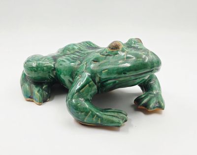 une figurine de grenouille verte posée sur une surface blanche