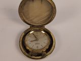 une petite montre de poche en or posée sur une surface blanche
