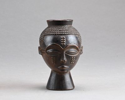 un vase noir orné d'un visage, posé sur une table