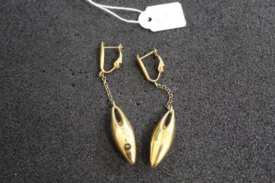 une paire de boucles d'oreilles en or posées sur une surface noire, avec une étiquette de prix