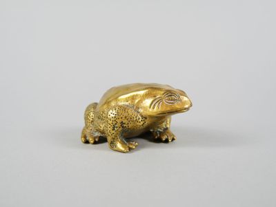 une figurine de grenouille dorée posée sur une surface blanche