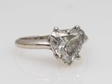 a close up of a heart shaped diamond ring on a white surface