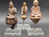 trois figurines asiatiques représentant des bouddhas, exposées sur des socles en acrylique transparent