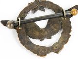 a metal brooch with a stick in the middle of it