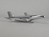 maquette d'avion en métal argenté posée sur une surface blanche, avec un fond gris