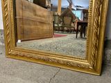 a gold framed mirror sitting on the floor in front of a dresser