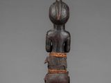 a wooden statue of a woman with a large head and hands on her chest