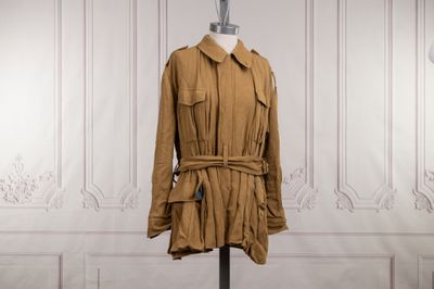 un trench-coat marron posé sur un mannequin devant un mur blanc