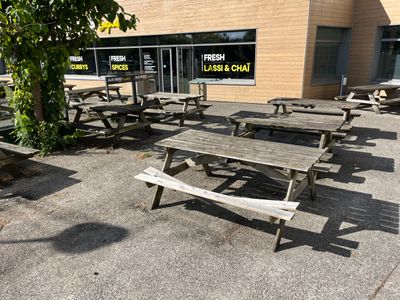 des tables et des bancs devant un bâtiment où est accrochée une enseigne indiquant « poisson frais et frites »