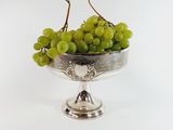 a silver bowl with grapes in it on a white surface