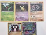 Plusieurs cartes Pokémon sont posées sur une surface blanche, sur fond blanc.