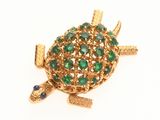 une photo d'une broche en forme de tortue en or, ornée de pierres vertes et bleues