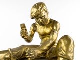 a gold statue of a man sitting on the ground holding a cell phone