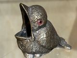 figurine en argent représentant un oiseau aux yeux rouges posé sur une table