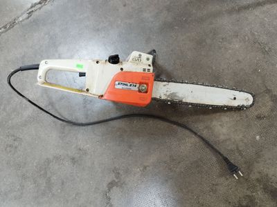 une tronçonneuse orange et blanche posée sur un sol en béton
