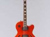 an orange electric guitar hanging from a string on a white wall