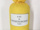 un flacon jaune du parfum « Eau de Monsieur Balmain » posé sur une surface blanche