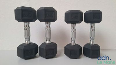 trois haltères hexagonaux en caoutchouc noir posés sur une table blanche