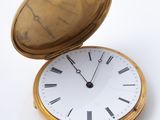 une montre de poche en or posée sur une surface blanche