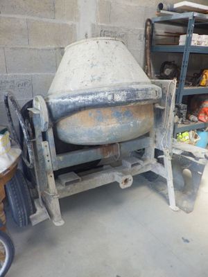 une bétonnière posée dans un garage, à côté d'une étagère où sont rangés d'autres objets