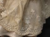 a close up of a doll wearing a white dress and holding a teddy bear