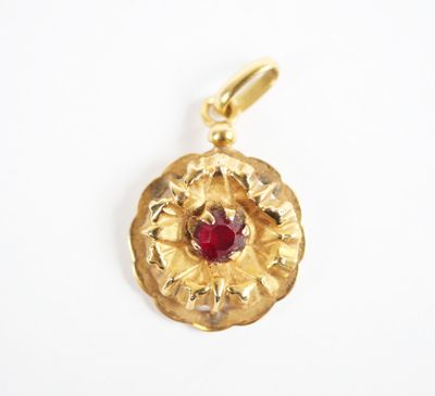 a close up of a gold pendant with a red stone