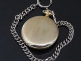 a silver pocket watch on a chain on a black surface