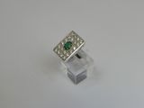 an emerald and diamond ring on a clear acrylic stand