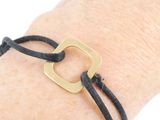 black leather bracelet with a brass square on a hand