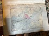 an old map of a city on a table with a person holding it