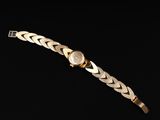 a gold bracelet with a watch on a black background
