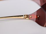 sunglasses with a gold rim and a red lens on a white surface