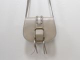beige leather handbag with silver hardware and tassels hanging on a white wall