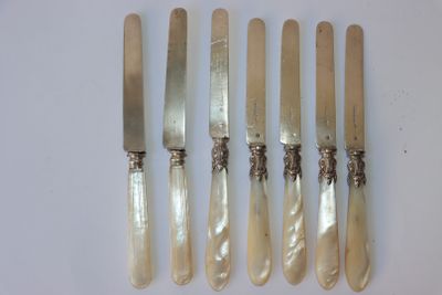 six couteaux et un porte-couteaux sont alignés sur une surface blanche