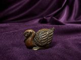 a small bronze duck figurine sitting on a purple cloth