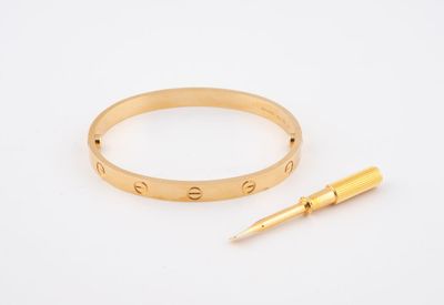 un gros plan d'un bracelet en or et d'un stylo posés sur une surface blanche