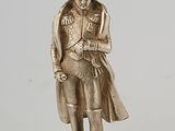 figurine en argent représentant un homme portant un chapeau et un manteau, posée sur un socle