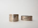 two silver rings with engraved designs on them sitting on a white surface