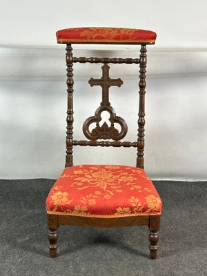 une vieille chaise en bois avec une assise rembourrée rouge et une croix sur le dossier
