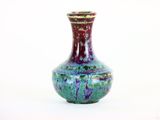 un vase violet et vert posé sur une surface blanche