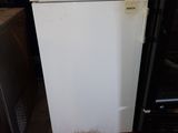 a white refrigerator sitting in a warehouse next to a black refrigerator
