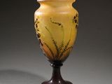 yellow and brown glass vase on stand against a gray background