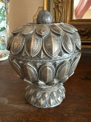un vase en argent posé sur une table, avec un miroir en arrière-plan