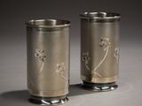 two silver cups with flowers on them sitting on a table