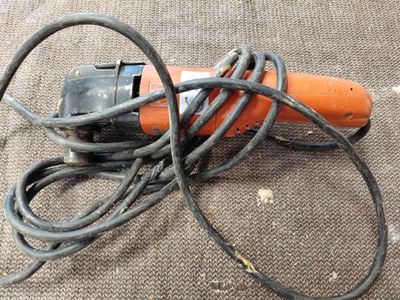 une perceuse électrique orange et noire posée par terre