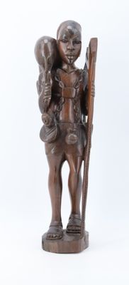 une vieille statue en bois représentant un homme tenant un bâton et un sac
