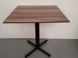 a square wooden table with a black metal cross base