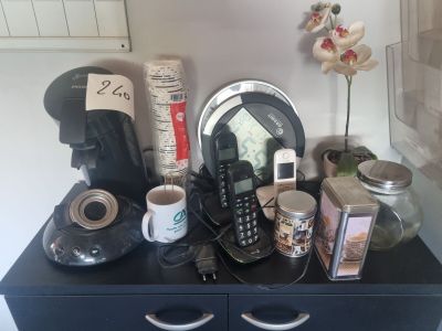 une commode noire sur laquelle sont posés un téléphone, des tasses à café et d'autres objets