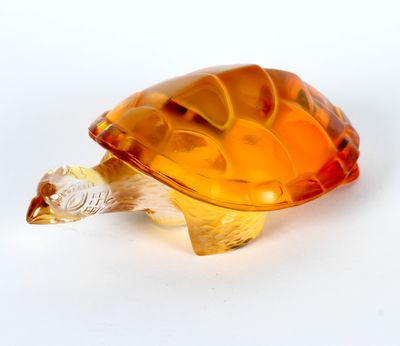 une figurine de tortue en verre orange posée sur une surface blanche