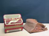un petit accordéon rouge et un sac marron posés sur une table